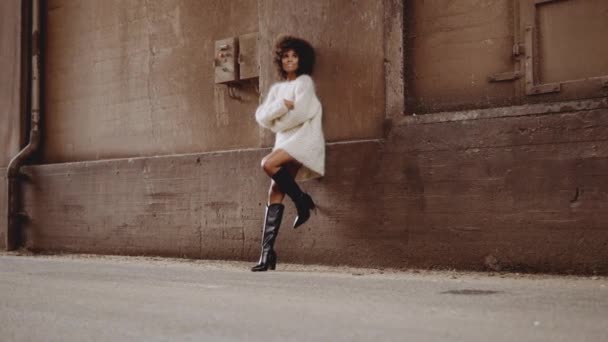 Donna sorridente con vento spazzato afro in abito di lana e stivali con tacco alto — Video Stock