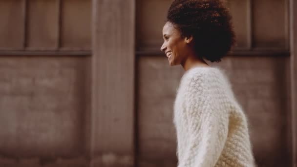 Lächelnde junge Frau mit windgebeugten Afro-Haaren, die die Straße entlang läuft — Stockvideo