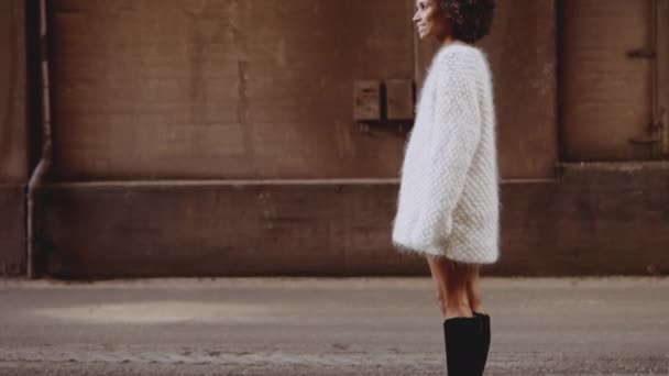 Χαμογελώντας νεαρή γυναίκα με ανεμοδαρμένο αφρό μαλλιά στέκεται στο δρόμο — Αρχείο Βίντεο