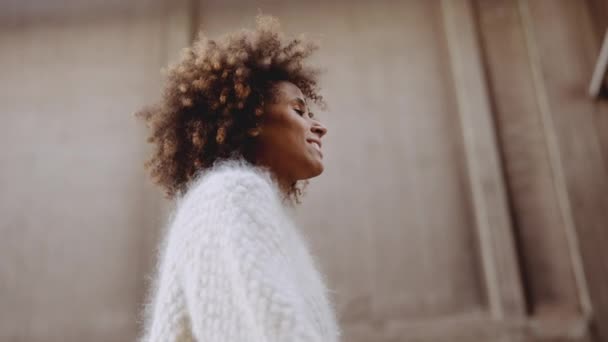 Lächelnde junge Frau mit windgebeugten Afro-Haaren, die die Straße entlang läuft — Stockvideo