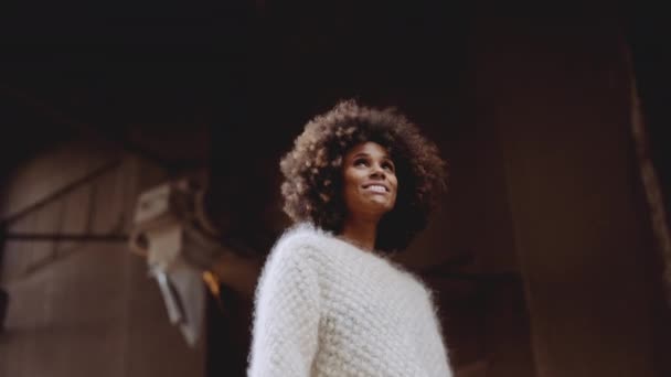 Jeune femme souriante avec des cheveux afro balayés par le vent marchant le long de la rue — Video