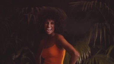 Gülümseyen ve kameraya afro saç takan genç bir kadın.