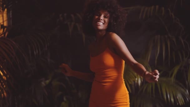Afro saçlı gülümseyen kadın turuncu elbiseli kamerayla dans ediyor. — Stok video