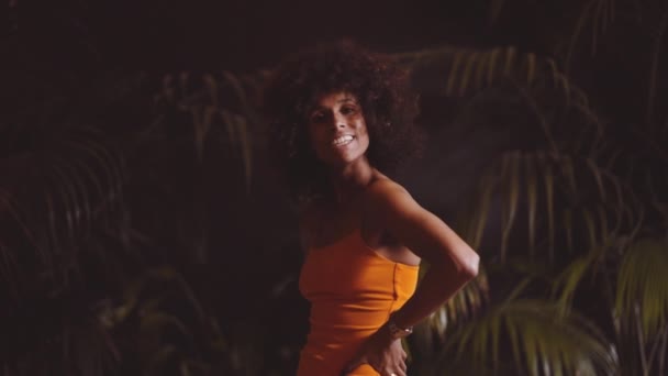 Afro gülüşlü ve turuncu elbiseli kameraya tavır takınan bir model. — Stok video