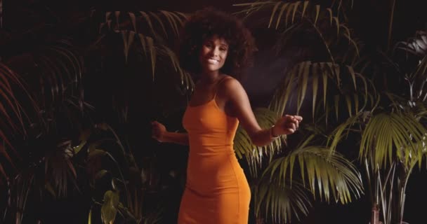 Afro saçlı, turuncu elbiseli, kamerayla dans eden genç bir kadın. — Stok video