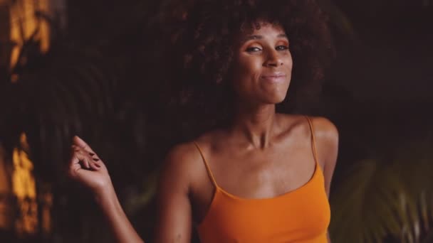 Jonge vrouw glimlachen en dansen naar camera in oranje jurk — Stockvideo