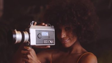 Turuncu saçlı, gülümseyen kadın klasik kamera kullanıyor.