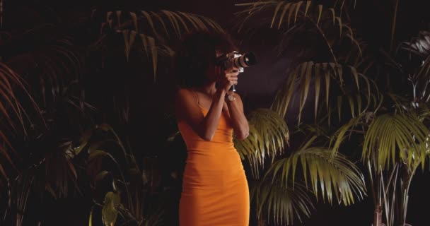 Женщина с африканскими волосами в оранжевом платье с помощью винтажной 8-мм камеры — стоковое видео