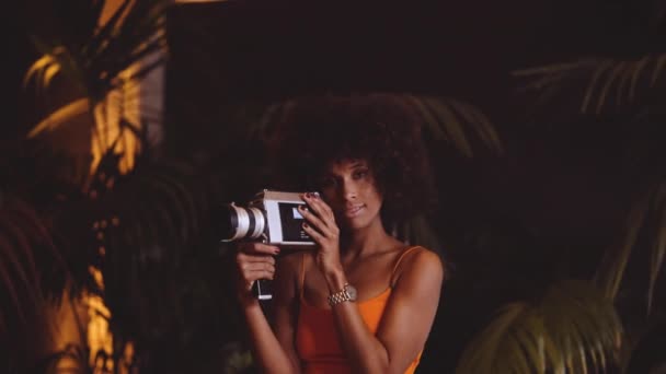 Mujer con pelo afro en vestido naranja celebración de la vendimia 8mm cámara — Vídeos de Stock
