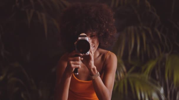 Mujer con pelo afro en vestido naranja con cámara vintage de 8mm — Vídeos de Stock