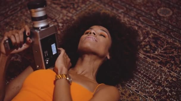 Mujer con pelo afro en vestido naranja con cámara vintage de 8mm — Vídeos de Stock