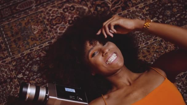 Mujer con cabello afro sonriendo en el piso con cámara vintage de 8mm — Vídeo de stock