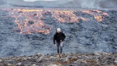 Sırt çantasını çıkartan adam arkasında lav akarken