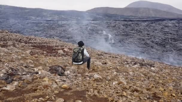 Fotógrafo sentado en la roca por el campo de lava — Vídeos de Stock