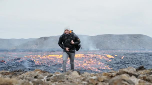 Hombre quitándose la mochila mientras la lava fluye detrás de él — Vídeo de stock