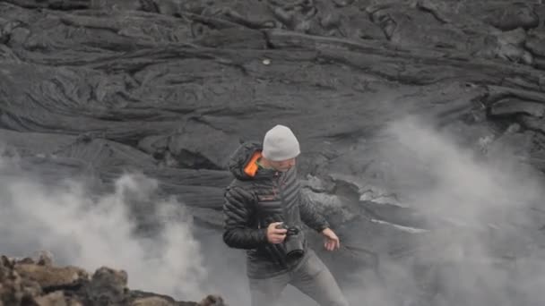 Fotógrafo celebración de la cámara entre fumar campo de lava — Vídeos de Stock