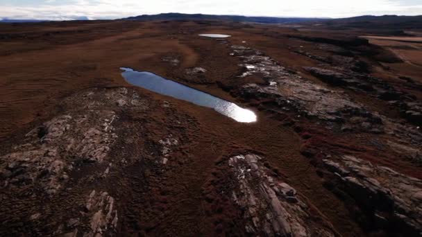 Drone vlucht over rotsen in landschap met meren die zonlicht reflecteren — Stockvideo