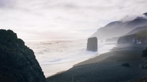Misty zwarte zand strand met zee stapel en witte branding — Stockvideo