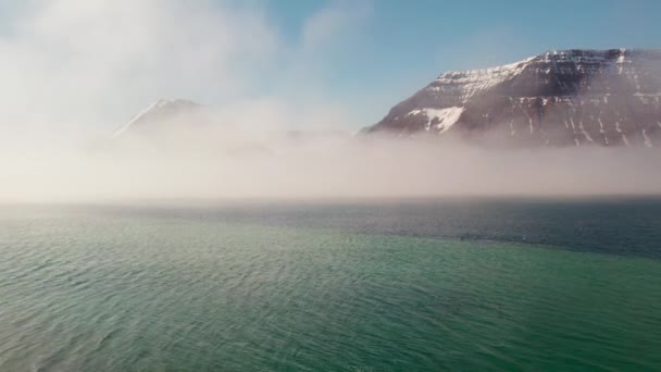 Voo de drone em direção a montanhas nebulosas com neve sobre o fiorde — Vídeo de Stock