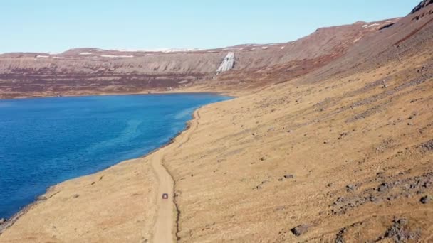 Bil på smutsspår genom fjorden mot vattenfall på berget — Stockvideo