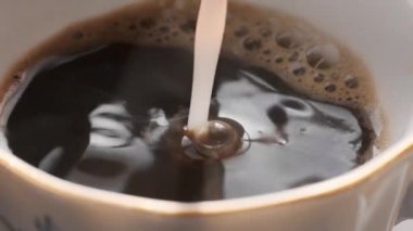 Sıcak kahve fincanda süt dökülüyor.