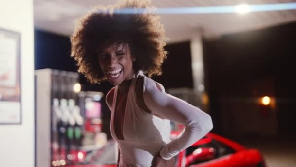 Donna con afro in tuta posa in distributore di benzina di notte — Video Stock