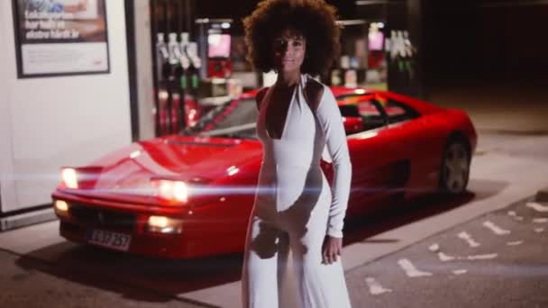Vrouw met afro in jumpsuit poseren door Ferrari 348 in tankstation — Stockvideo