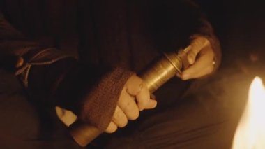 Geceleri mağaradaki kamp ateşinde eski kahve öğütücüsünün tepesinde kıvrılan adam.