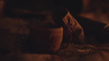 Geceleri karanlık mağarada kamp ateşinin yanında fincan ve poşet.