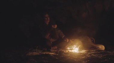 Karanlık Mağarada Kamp ateşiyle aydınlatılan Kupa İçen Adam