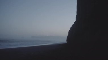 Uzak deniz feneri manzaralı mağaradan Kara Kumsala karşı dalgalar