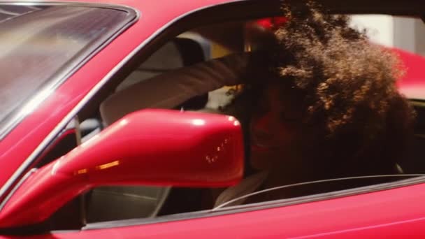 Kvinna med afro sitter i förarsätet av röd bil — Stockvideo
