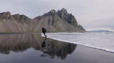 Sırtında üç ayaklı adam Vestrahorn sahilinde sörf yapıyor.