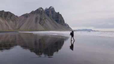 Sırt çantalı bir adam Islak plajda yürüyor Vestrahorn 'dan denize doğru