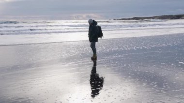 Sırt çantalı adam Islak plajda yürüyor