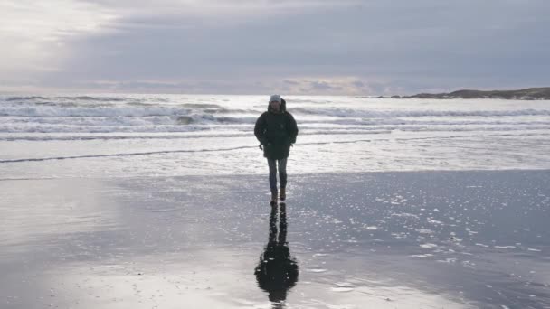 Άνθρωπος περπατώντας κατά μήκος ηλιοφωτισμένη υγρή παραλία προς την κάμερα — Αρχείο Βίντεο