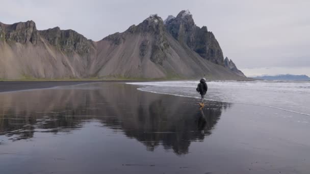Hombre con mochila caminando por la playa húmeda hacia el mar por Vestrahorn — Vídeos de Stock