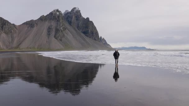 Άντρας με σακίδιο περπατώντας κατά μήκος βρεγμένη παραλία από Vestrahorn Mountain — Αρχείο Βίντεο