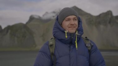 Arka planda Vestrahorn Dağı, İzlanda 'dan denize bakan Mavi Giysili Adam' ın Yavaş Çekim El Fotoğrafı