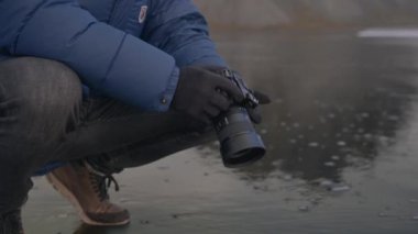 Islak plajda çömelmiş ve İzlanda 'da kameralı bir adamın orta ölçekli ağır çekim çekimi.