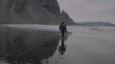Fotoğrafçının Black Sand Beach üzerinden denize ve Vestrahorn Dağı, İzlanda 'ya doğru yürüyüşünün geniş çaplı ağır çekim tecrit görüntüleri.