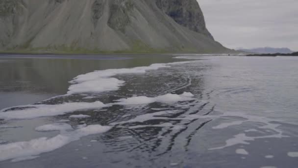 スローモーション アイスランドのヴェストラホーンビーチ近くの黒い砂のビーチに来る泡の潮のショット — ストック動画