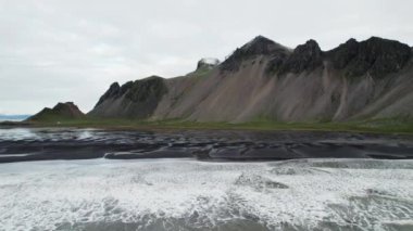 Wide Slow Motion İHA uçağı denizden, Black Sand Beach 'ten ve Vestrahorn Dağı, İzlanda' dan ayrılıyor.
