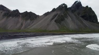 Wide Arcing Slow Motion Flight Over Sea, Black Sand Beach ve Vestrahorn Mountain, İzlanda