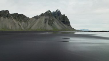 Wide Slow Motion Drone Islak Kum Kumsalı üzerinden İzlanda 'daki Vestrahorn Dağı' na doğru uçuyor.
