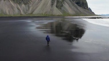 Yavaş Hareketli İHA Uçuşu Kara Kum Kumsalı 'nda Yürüyen, Kamerayı tutan İzlanda, Vestrahorn Dağı' na doğru