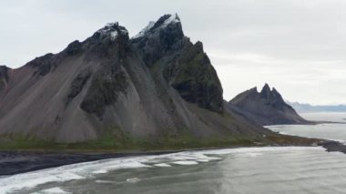 Geniş Yavaş Hareketli İHA Uçuşu Deniz Üzerinde, Kara Kum Kumsalı ve Vestrahorn Dağı, İzlanda