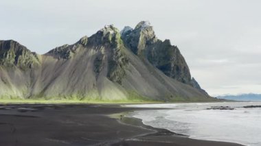 İzlanda, Vestrahorn Dağı 'na doğru gelen dalgalarla Kara Kum Sahili' nde Yürüyen Adam 'ın İHA görüntüsü