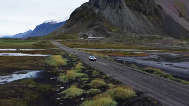 アイスランドの風景の中に湿式ダートトラック道路に沿って車の運転の広い追跡ドローン飛行ベストラホーン山 — ストック動画