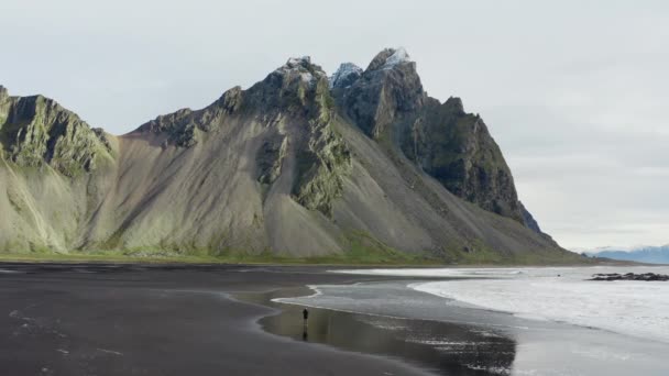 スローモーション黒砂のビーチで男の静的ドローンショット潮がベストラホーン山の下に来て アイスランド — ストック動画